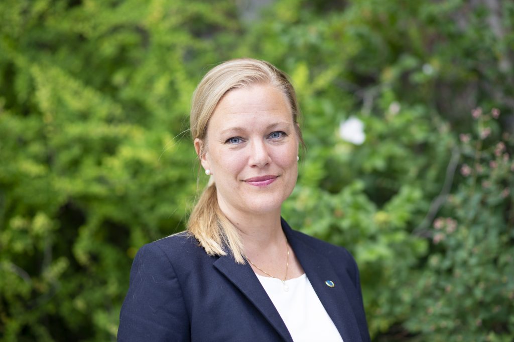 FN-förbundets ordförande Annelie Börjesson. Annelie har en mörkblå kavaj och står framför en grön buske