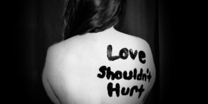 Kvinnas axel med texten Love shouldn't hurt