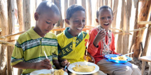 Tre pojkar äter skolmat i Etiopien.