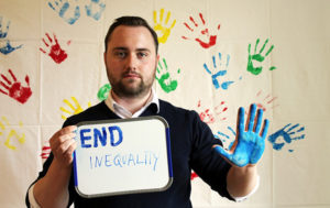 Albert Askelljung, fd anställd på Svenska FN-förbundet och nu anställd på UNDP, håller fram en skylt "End Inequality" framför ett lakan med handavtryck.