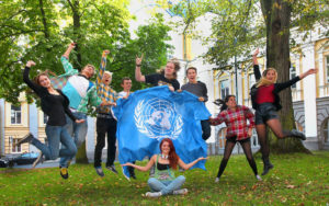 Ungdomar hoppar med en FN-flagga på en FN-skola