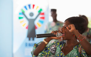 Kvinna håller tal med Agenda 2030-symbolen i bakgrunden. Foto: UN Photo