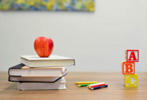 Böcker, pennor, klossar och ett äpple i ett klassrum. Foto: Unsplash