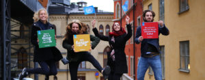 Gruppbild på ungdomar som hoppar upp i luften och håller i skyltar om de globala målen och Svenska FN-förbundets flaggor