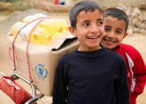 Två leende pojkar i Syrien framför ett matpaket från WFP