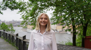 Julia tittar in i kameran och ler med Stockholm stad bakom sig
