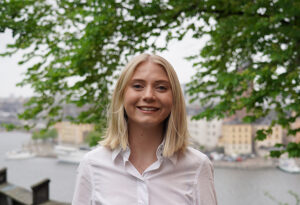 Julia tittar in i kameran och ler med Stockholm stad bakom sig