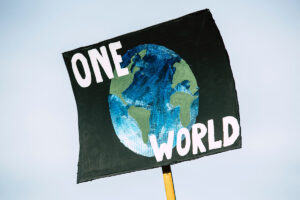 Bild på en skylt med en målad jordglob på svart botten. Texten på skylten lyder One World.