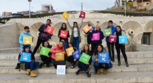 Ett gäng ungdomar står på en trappa och håller glatt upp färgglada globala målen-skyltar