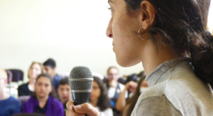 En person är i fokus och håller i en mikrofon framför en publik