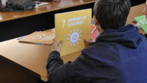 En ungdom sitter vid ett bord och håller i en gul skylt med globala målet 7 i sin hand.