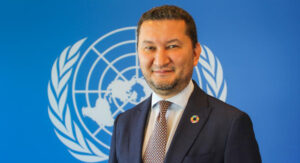 Porträttbild på Toily Kurbanov (chef för UNV), framför FN-flaggan.