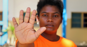 Fátima Issufo de Carvalho från organisationen PROMURA deltar i en manifestation mot våld mot kvinnor i samband med en konferens om kvinnor, fred och säkerhet i Pemba City, Mocambique, i november 2022. På bilden står hon och håller upp handen i en stoppgest iklädd orange T-shirt.