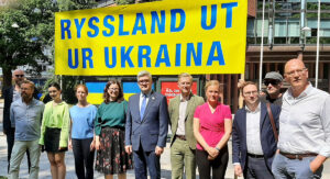 Talarna vid onsdagens manifestation står framför en gul skylt med texten Ryssland ut ur Ukraina. Ukrainas ambassadör i Sverige, Andrij Plachotnjuk, står i mitten och FN-förbundets ordförande Annelie Börjesson syns i rosa till höger i bild.